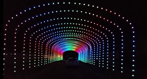 A colorful illuminated tunnel with vibrant lights in an arch pattern, leading to a dark entrance.