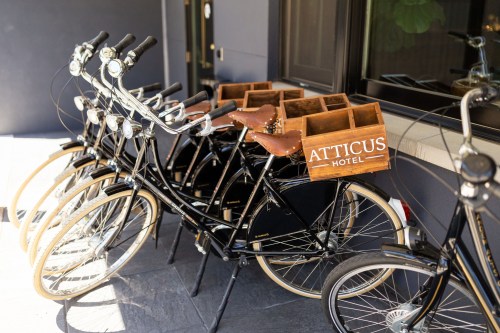 A row of black bicycles with wooden baskets labeled "ATTICUS HOTEL" parked outside a building.