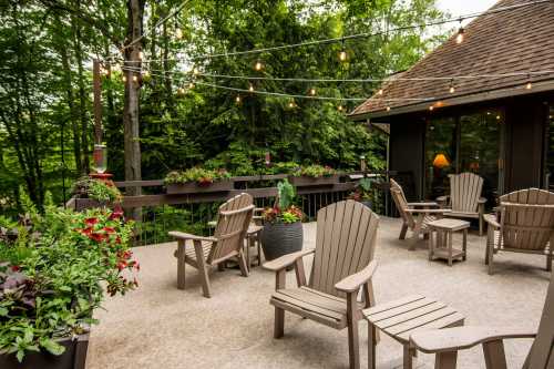 A cozy outdoor patio with wooden chairs, potted plants, and string lights, surrounded by lush greenery.