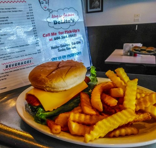 A cheeseburger with lettuce and a slice of cheese, served with crinkle-cut fries, next to a menu.