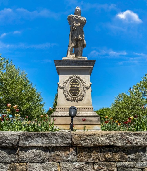 Statue of Simon Bolivar on a stone pedestal, surrounded by flowers and trees under a clear blue sky.