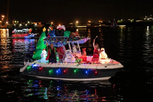 A decorated boat with festive lights and holiday figures, sailing on water at night during a holiday celebration.