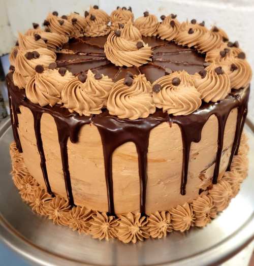 A decadent chocolate cake with swirls of frosting, chocolate ganache drips, and chocolate chips on top.