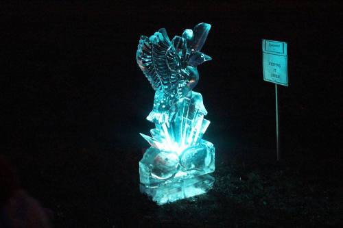 An illuminated ice sculpture of an eagle perched on crystals, glowing in blue light against a dark background.