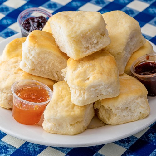 A plate of fluffy biscuits served with small cups of orange and berry jams on a blue checkered tablecloth.