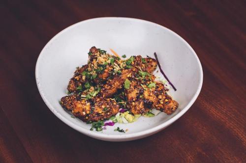 A bowl of crispy chicken wings garnished with herbs and served on a bed of colorful slaw.