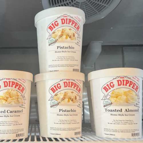 Four tubs of "Big Dipper" ice cream in flavors: Pistachio, Toasted Almond, and Caramel, displayed in a freezer.