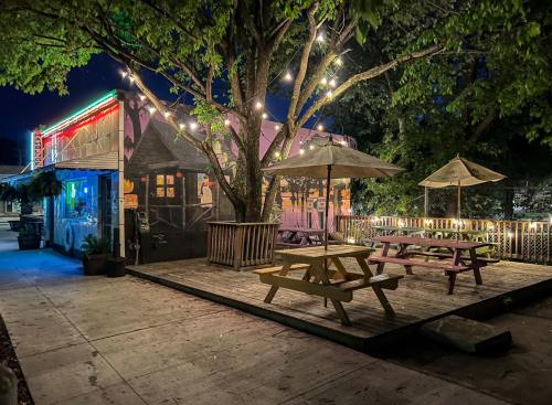 A cozy outdoor dining area at night, featuring picnic tables, umbrellas, and string lights around a tree.