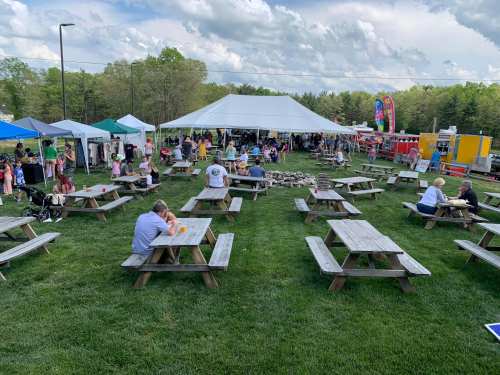 A lively outdoor event with tents, picnic tables, and people enjoying food and activities on a grassy field.