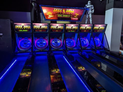 A brightly lit skee ball arcade game with multiple lanes and a stormtrooper figure in the background.
