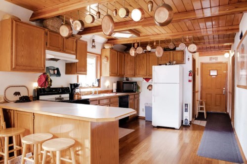 A cozy kitchen with wooden cabinets, a white refrigerator, and hanging pots, featuring a warm, inviting atmosphere.