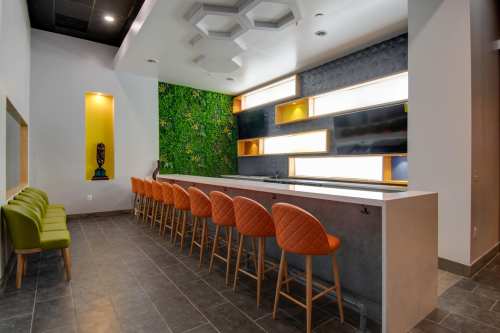 Modern bar area with orange stools, green wall accents, and a sleek countertop in a stylish interior space.