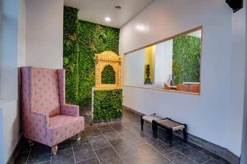 A cozy interior with a pink armchair, greenery wall, and a decorative archway on a tiled floor.
