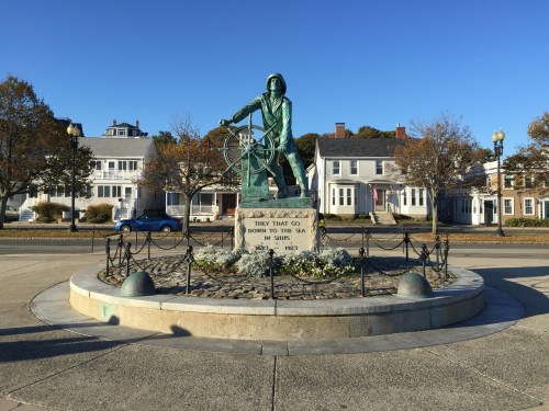 A bronze statue of a fisherman at a wheel, surrounded by a landscaped area and historic buildings in the background.