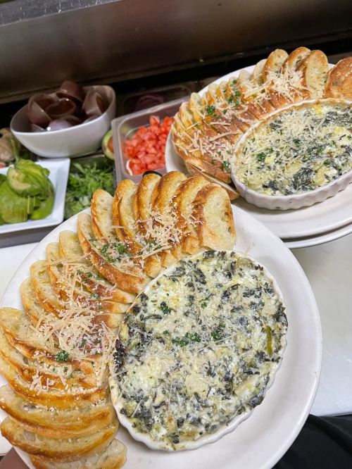 Two plates of baked spinach dip surrounded by toasted bread slices, garnished with herbs and cheese.