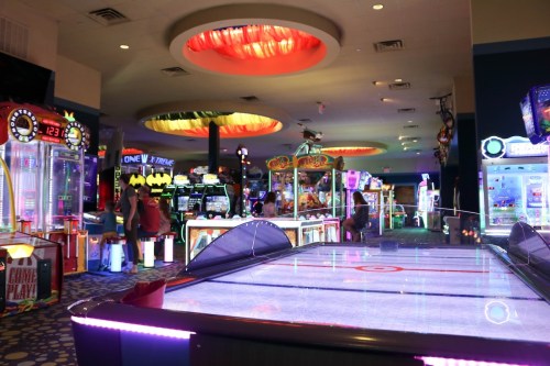 A vibrant arcade filled with colorful games and bright lights, featuring air hockey and various arcade machines.