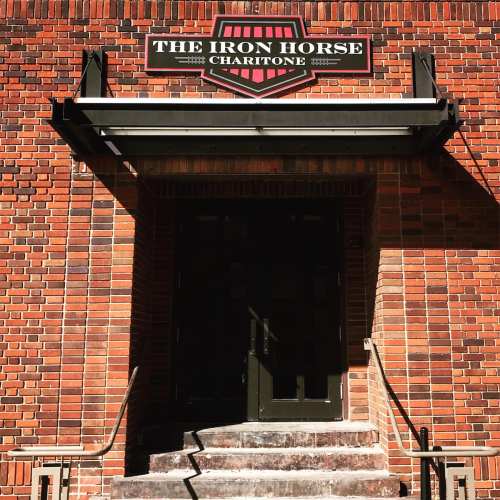 Sign for "The Iron Horse" above a doorway, set against a brick wall. Sunlight casts shadows on the entrance.