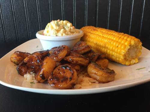 A plate featuring grilled shrimp, corn on the cob, and a side of creamy potato salad.