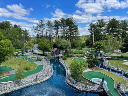 A scenic mini-golf course with lush greenery, water features, and blue skies dotted with clouds.
