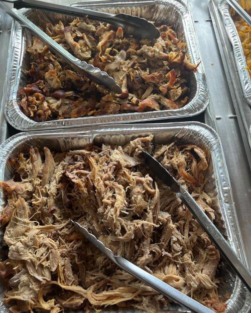 Two trays of shredded pulled pork with tongs, showcasing tender, flavorful meat.