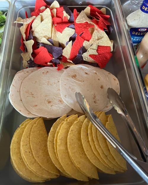 A tray of colorful tortilla chips, flour tortillas, and corn tortillas, with tongs for serving.