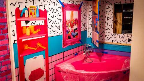 A colorful bathroom with bright pink walls, a bathtub, and playful decor featuring geometric patterns and vibrant accessories.