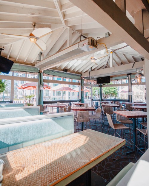 Bright, airy restaurant interior with wooden beams, tables, and chairs, featuring large windows and a relaxed atmosphere.