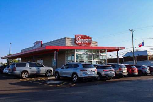 Exterior of Svensons restaurant with a red awning and parked cars in front, under a clear blue sky.