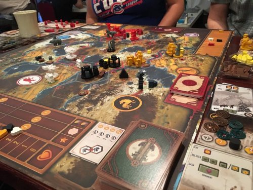 A tabletop game in progress, featuring a colorful game board, various tokens, and player cards.