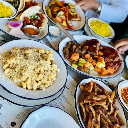 A table spread with various dishes, including macaroni and cheese, tacos, rice, and colorful vegetables.