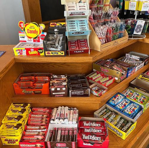 A display of various candies and snacks on wooden shelves, including chocolate bars and colorful treats.
