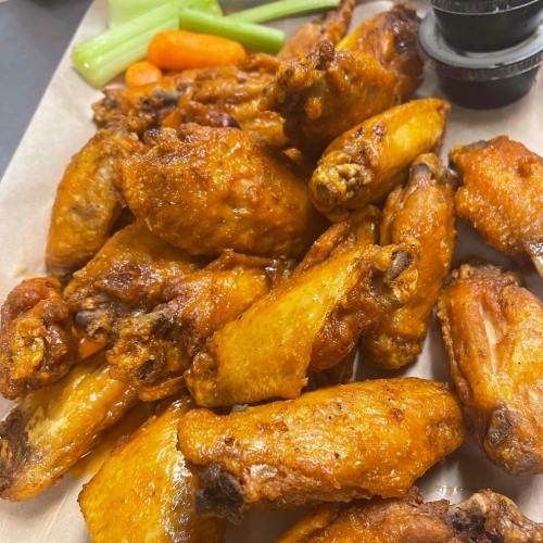 A plate of crispy chicken wings with celery and carrots, served with a small container of dipping sauce.