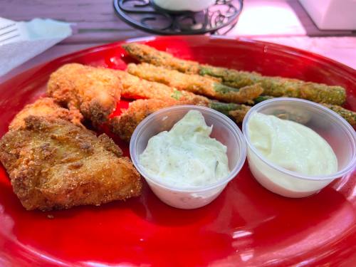 A red plate with fried shrimp, fish, and crispy asparagus, accompanied by two dipping sauces in small cups.