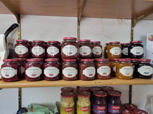 A shelf displaying various jars of jam and preserves, labeled with flavors like blueberry, cherry, and apricot.