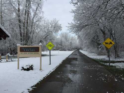 A snowy trail entrance with signs for biking and horseback riding, surrounded by trees and a quiet, winter landscape.