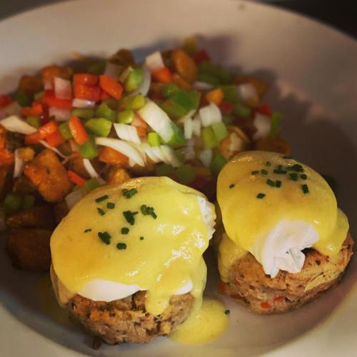 A plate featuring two eggs Benedict with hollandaise sauce, served with a side of colorful diced vegetables and potatoes.