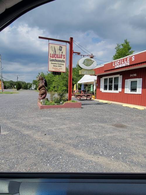 A roadside view of Lucille's Luncheonette, featuring a sign and a decorative sculpture outside the red building.