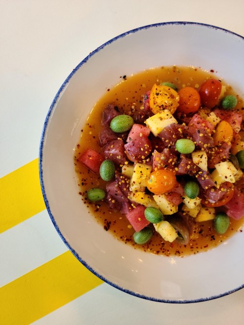A colorful bowl of salad with diced vegetables, fruits, and a tangy dressing, set against a light background.