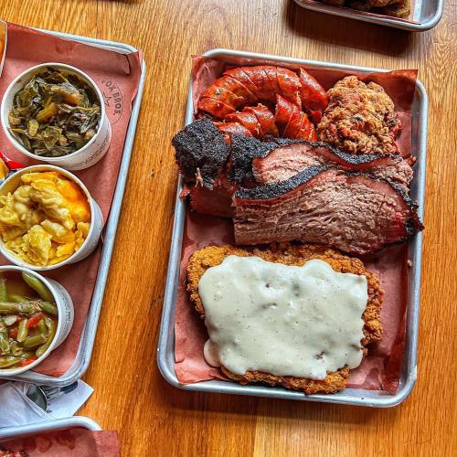 A metal tray with barbecue brisket, shrimp, fried chicken, and sides of collard greens, mac and cheese, and green beans.