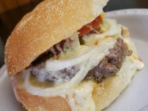 A close-up of a juicy hamburger with melted cheese, onions, and tomatoes, served in a toasted bun.