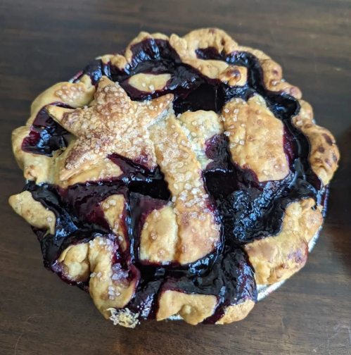 A baked pie with a star-shaped crust and a glossy berry filling, resting on a wooden surface.
