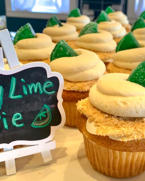 A display of key lime pie cupcakes topped with green candy and a chalkboard sign labeling them.
