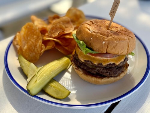 A juicy cheeseburger with lettuce, tomato, and pickles, served with crispy potato chips on the side.