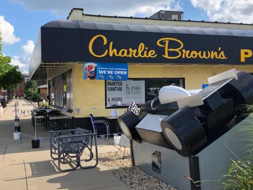 Exterior of Charlie Brown's restaurant with outdoor seating, signs indicating it's open, and decorative elements.