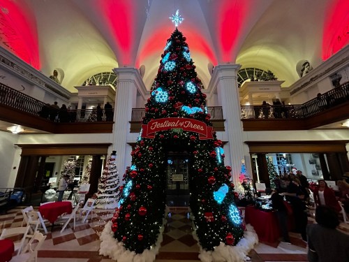 A beautifully decorated Christmas tree with red and blue lights, surrounded by festive decorations in a grand hall.