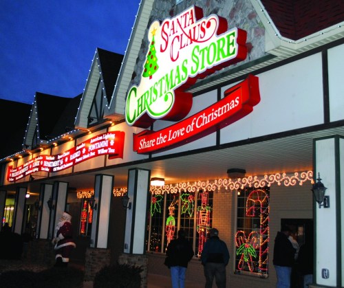A festive storefront with bright Christmas lights and decorations, featuring a sign that reads "Santa Claus Christmas Store."