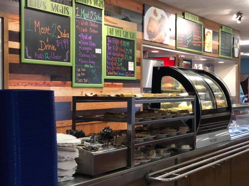 A cafeteria display with a menu board, showcasing meals and desserts in a warm, wooden setting.
