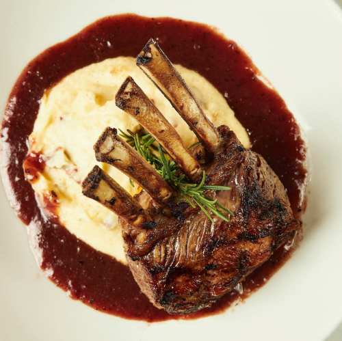 A beautifully plated lamb chop on creamy mashed potatoes, drizzled with red wine sauce and garnished with rosemary.