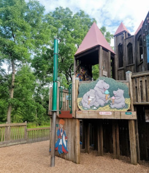 Playground structure with a slide, featuring a colorful mural of three bears enjoying ice cream, surrounded by trees.