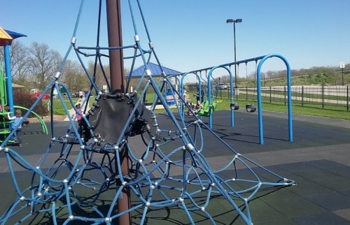 A playground featuring a climbing structure, swings, and a sunny blue sky in the background.